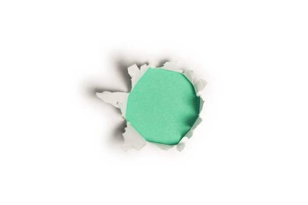 Un agujero en un papel blanco sobre un fondo verde, espacio para copiar.  - Foto, imagen