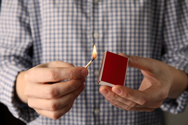 Man with box and burning match, closeup - Фото, изображение