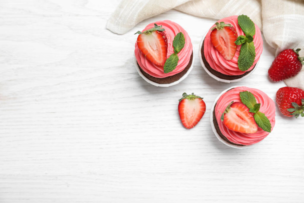 Sweet cupcakes with fresh strawberries on white wooden table, flat lay. Space for text - Фото, зображення