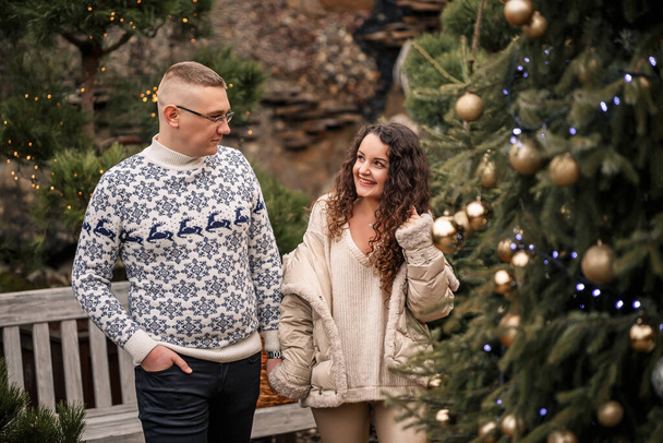 Χριστουγεννιάτικα κλαδιά ελάτης. Νεαρό ζευγάρι διακοσμεί ένα χριστουγεννιάτικο δέντρο έξω. Χριστουγεννιάτικα στολίδια, γλειφιτζούρια και μπάλες. - Φωτογραφία, εικόνα