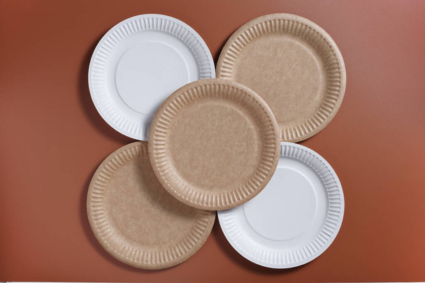 Одноразовые бумажные тарелки на коричневом фоне, вид сверху - Фото, изображение