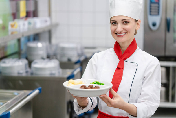 Cocinero mostrando plato con comida en cocina comercial de cantina - Foto, Imagen
