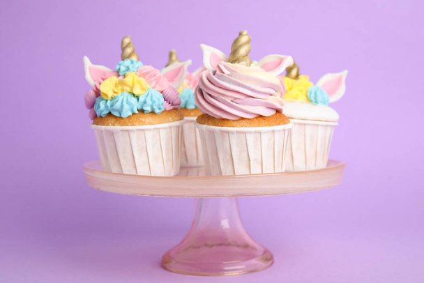 Cute sweet unicorn cupcakes on dessert stand against violet background - Foto, afbeelding