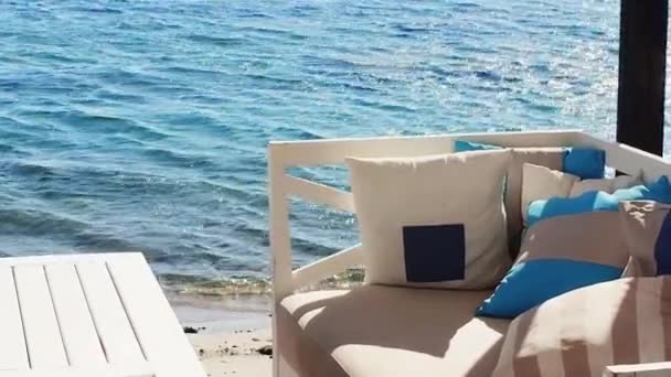 Ranta lounge ja kesäloma käsite. Valkoinen sohva mukavuutta tyynyt ja tyynyt ja pöytä lähellä sininen meri - Materiaali, video