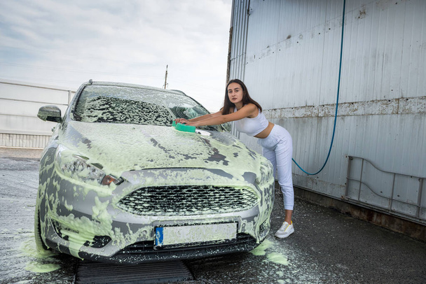 Yeşil süngerli, beyaz köpüklü, modern araba yıkayan güzel bir kadın sürücü. El işi araba yıkama servisi.. - Fotoğraf, Görsel