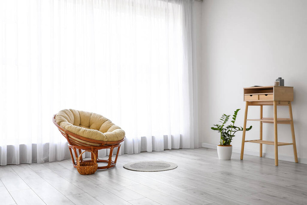 Armchair, stand-up table and houseplant near big window with light curtains - Foto, Imagem
