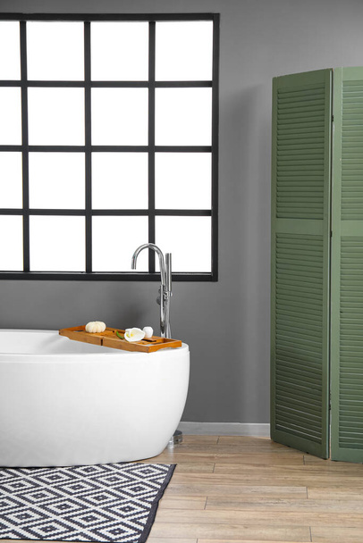 Интерьер серой ванной комнаты с большим окном и складным экраном - Фото, изображение