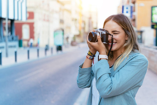 Smiling woman taking photo on camera in city - Zdjęcie, obraz