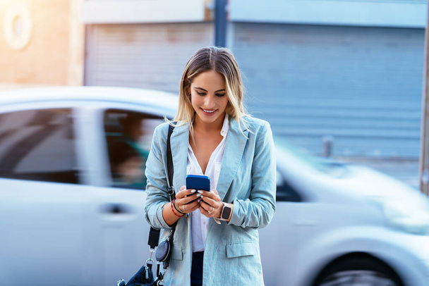 Cheerful stylish woman browsing cellphone in street - 写真・画像