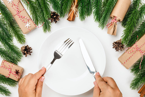 table set for Christmas party. Female hands hold a silver knife and fork over white empty plate - Foto, imagen