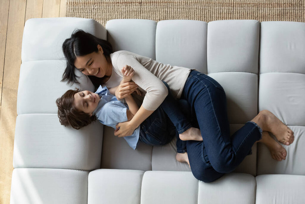Happy young Asian mom tickling and cuddling laughing son - Fotografie, Obrázek