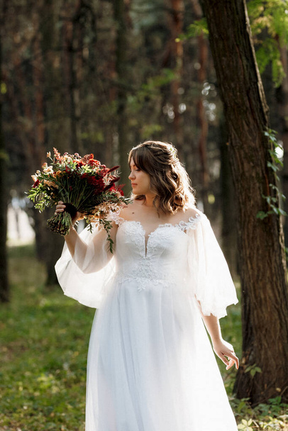 girl in a wedding dress in the autumn forest against the background of wild trees - Foto, imagen