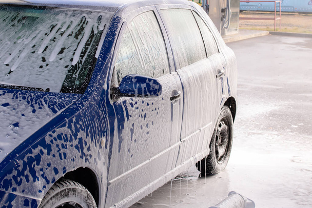 Blauwe auto in schuim bij een carwash close-up - Foto, afbeelding