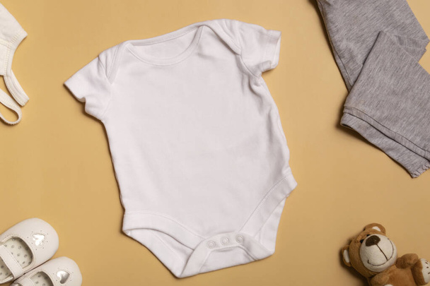 ロゴ、広告の設計と配置のためのモックアップ。白い赤ちゃんの体のスーツ、トップビュー、黄色の背景にモックアップ. - 写真・画像