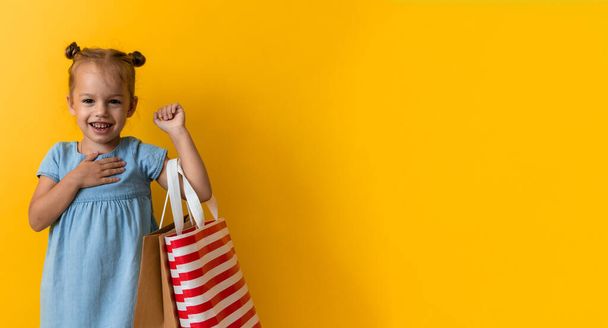 Banner Portrait Caucasian Beautiful Happy Little Preschool Girl Smiling Cheerful And Holding Cardboard Bags Isolated On Orange Yellow Background. Happiness, Consumerism, Sale People shopping Concept - Foto, immagini