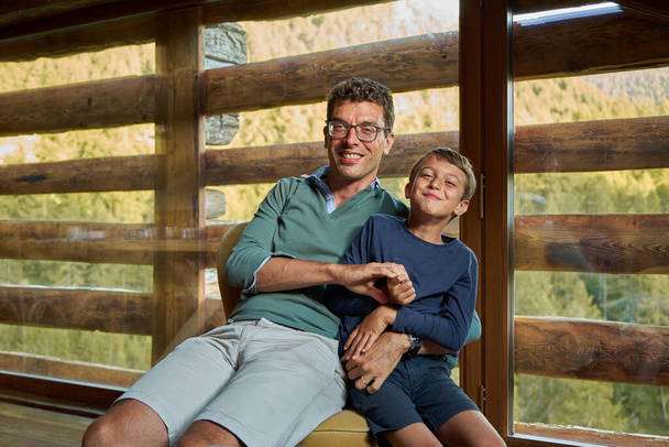 A young dad with glasses hugs his little brother sitting in a chair. - Fotó, kép
