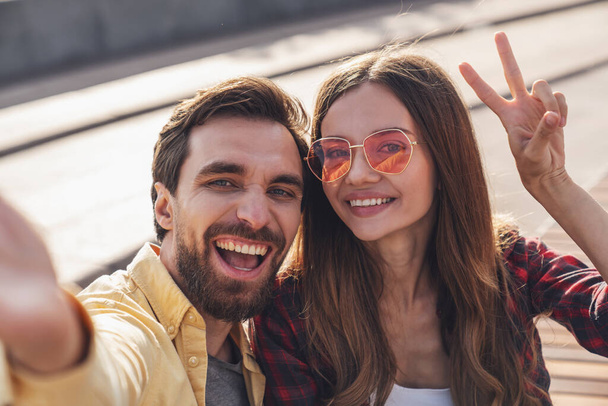 Jeune couple s'amuser à parler sur un banc et prendre un selfie en utilisant le téléphone tout en marchant dans la ville du matin. - Photo, image