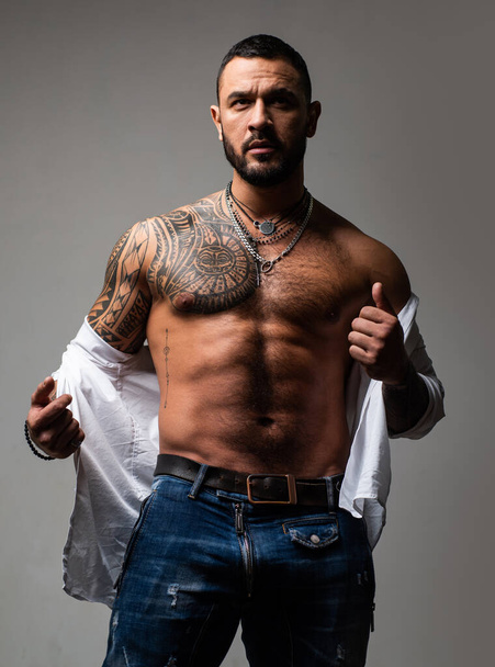 Brutal handsome man with tattooed body. Men tattoo casual fashion. Portrait of brutal handsome male model. Muscular athletic sexy male in unbuttoned shirt. Handsome guy with sexy bare torso. - Foto, Imagen