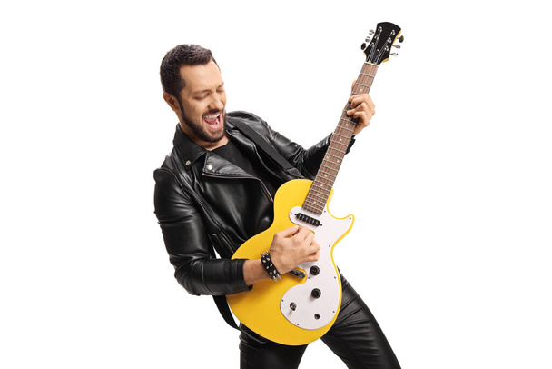 Young male musician in leather jacket and pants playing an electric guitar isolated on white background  - Valokuva, kuva