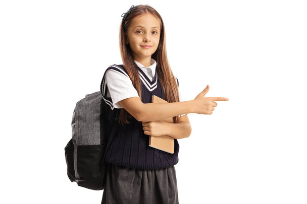 Schoolgirl with a backpack holding a book and pointing isolated on white background - Foto, immagini