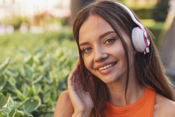 Young beautiful girl listens to music on headphones sitting on a park bench. - Foto, Bild