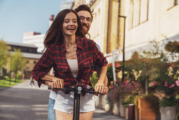 Jovem casal alegre enquanto monta uma scooter elétrica em uma rua da cidade. - Foto, Imagem