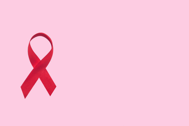 Red ribbon symbol of world aids day on pink background with copy space - Photo, Image