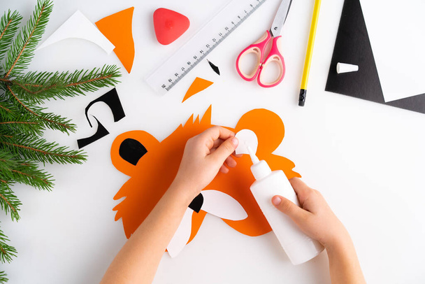 proces tworzenia maski tygrysa noworocznego dla dzieci z dzieckiem z kolorowego papieru, widok z góry, symbol 2022, krok 4. - Zdjęcie, obraz