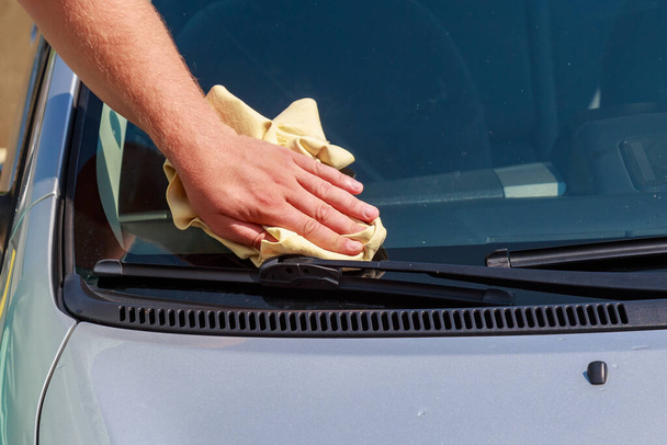 A hand with a dry rag wipes the windshield of a car at a car wash. Background with copy space for text or lettering. - Foto, Imagen