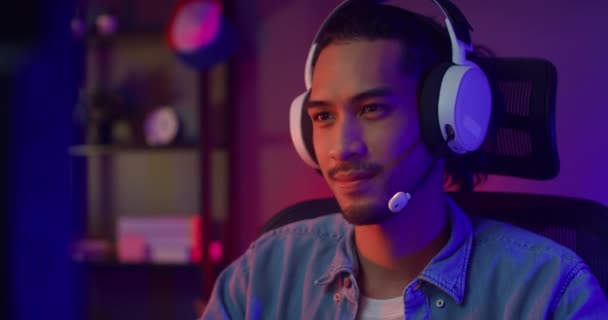 Boldog ázsiai srác játékos visel fejhallgató részvétel játék videojáték színes neon fények számítógép a nappaliban éjjel modern ház. Esport streaming játék online, Home karantén tevékenység koncepció. - Felvétel, videó