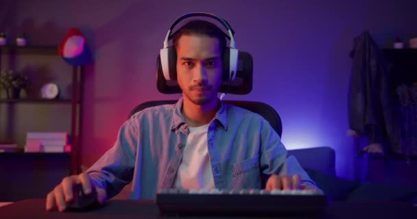 Boldog ázsiai srác játékos visel fejhallgató részvétel játék videojáték színes neon fények számítógép a nappaliban éjjel modern ház. Esport streaming játék online, Home karantén tevékenység koncepció. - Felvétel, videó