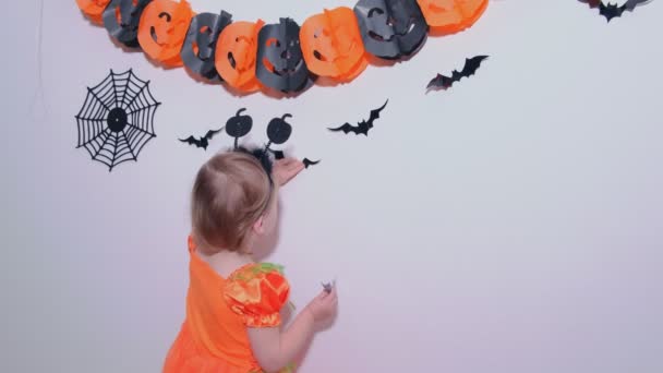 4k. Little girl in Pumpkin costume preparing for Halloween Decorating wall in room by black bats. - Footage, Video