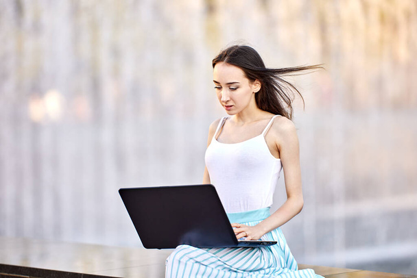 Slender woman is making telework using laptop outdoors. - Foto, Imagen