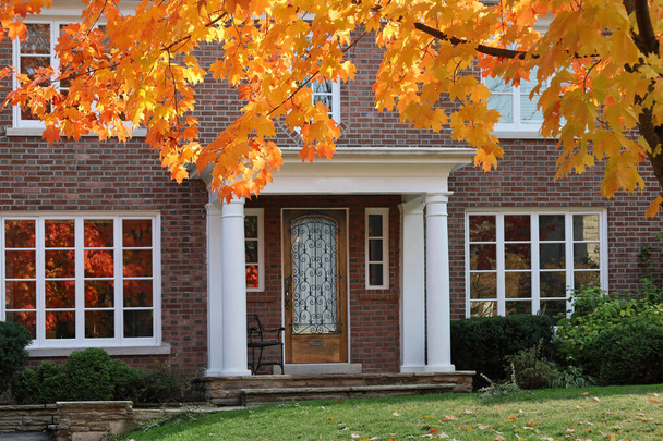 вхідні двері традиційного двоповерхового цегляного будинку з кленовим деревом у блискучому осінньому кольорі
 - Фото, зображення