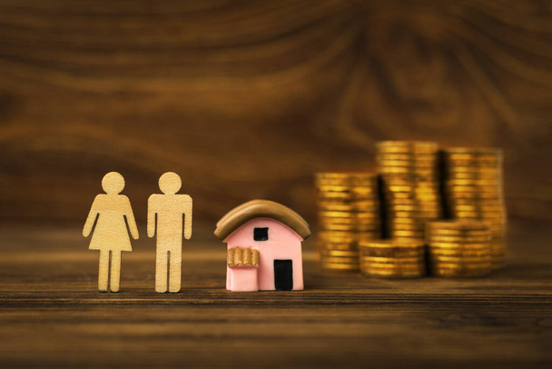 Monedas, un modelo de casa y figuras de madera masculina y femenina sobre un fondo de madera. El concepto de adquisición de vivienda. Hipoteca. - Foto, imagen