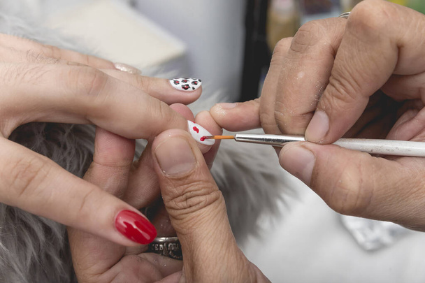 Peindre des taches de léopard rouge et noir sur un ongle poli avec un pinceau très fin. Procédure ongles art et touches de finition. - Photo, image
