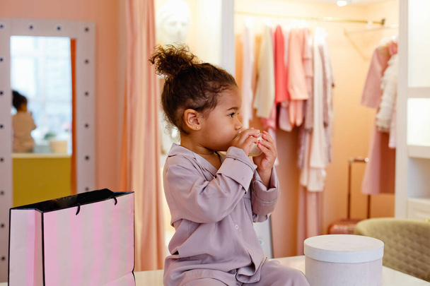 Söpö afroamerikkalainen tyttö makuuhuoneessa vaaleanpunaisessa pyjamassa. Söpö tyttö pukuhuoneessa. Söpö pieni tyttö äitinsä huoneessa. - Valokuva, kuva