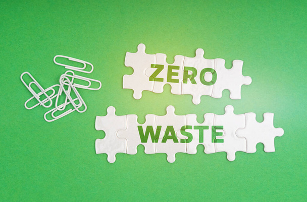 Ecology concept. On a green background, paper clips and white puzzles with the inscription - zero waste - Φωτογραφία, εικόνα