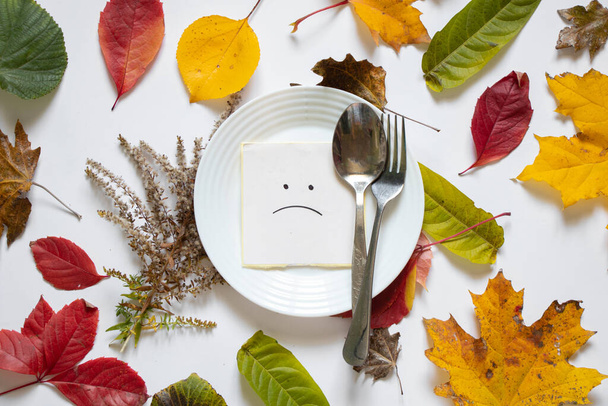 triste sonriente es dibujado sobre papel yace en un plato blanco sobre una mesa blanca en otoño hojas amarillas, tristeza tristeza depresión, crisis no tiene nada que comer - Foto, imagen