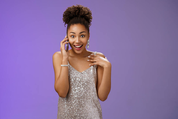 Impressed talkative charming african-american woman in shiny silver evening dress pointing herself amused surprised smiling talking smartphone widen eyes astonished, standing blue background - Photo, Image