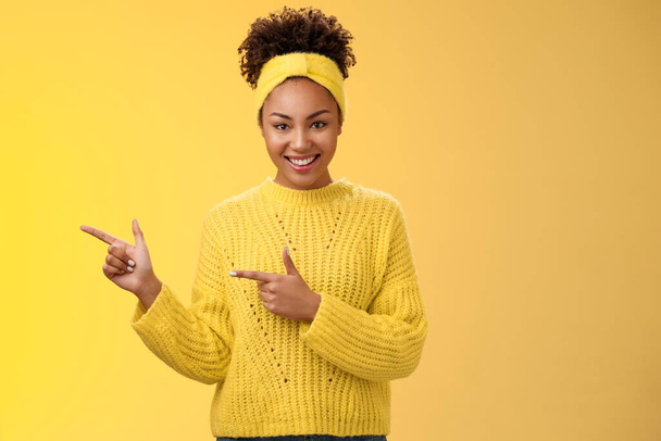Selbstbewusst gut aussehende Millennial feminine afrikanisch-amerikanische Frau Stirnband-Pullover aussehen selbstbewusst selbstbewusst zeigt den linken Zeigefinger wird es Ihnen gefallen lächeln, stehend gelben Hintergrund - Foto, Bild