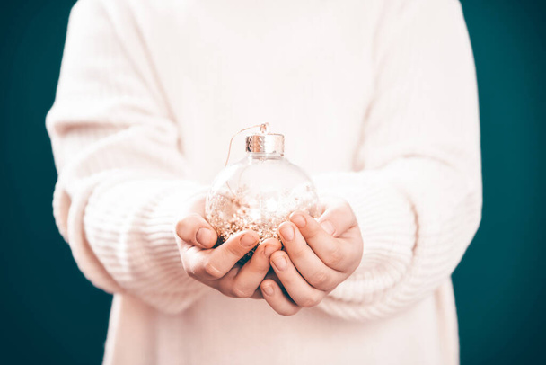 Klein meisje in de winter trui houdt in haar handen een kerstbal. - Foto, afbeelding