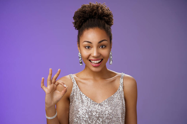 Everything alright. Portrait friendly elegant attractive smiling happy african woman in silver fashionable dress show okay no problem gesture grinning ok sign, standing blue background - Photo, Image