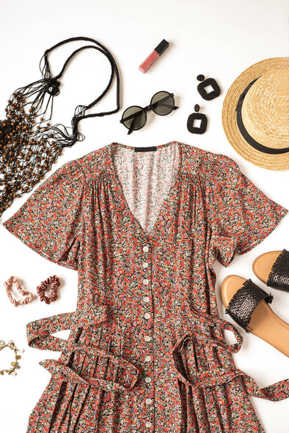 Vrouwelijke zomer esthetische kleding compositie met sundress, slippers, zonnebril, strohoed, string bag, oorbellen op witte achtergrond. Vlakke lay, bovenaanzicht minimaal doek concept - Foto, afbeelding
