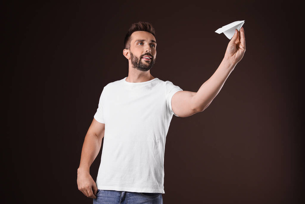 Hombre guapo jugando con avión de papel sobre fondo marrón - Foto, Imagen