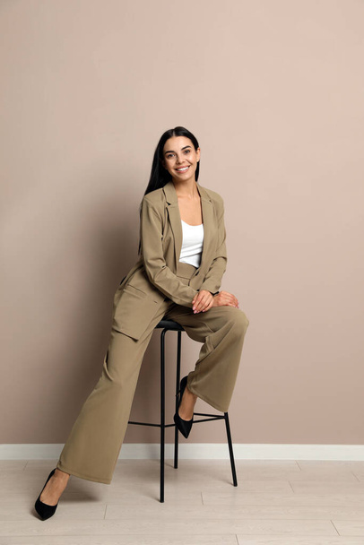 Beautiful young businesswoman sitting on stool near beige wall - Zdjęcie, obraz