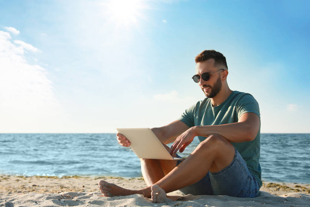 Mann arbeitet mit Laptop am Strand. Raum für Text - Foto, Bild