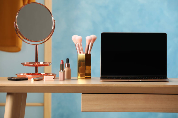 Wooden table with modern laptop and makeup products in room - Φωτογραφία, εικόνα