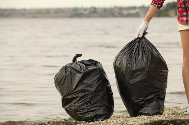Woman with trash bags full of garbage on beach, closeup - Fotoğraf, Görsel
