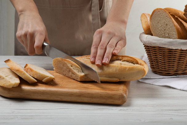 Woman cutting freshly baked baguette at white wooden table, closeup - Fotografie, Obrázek